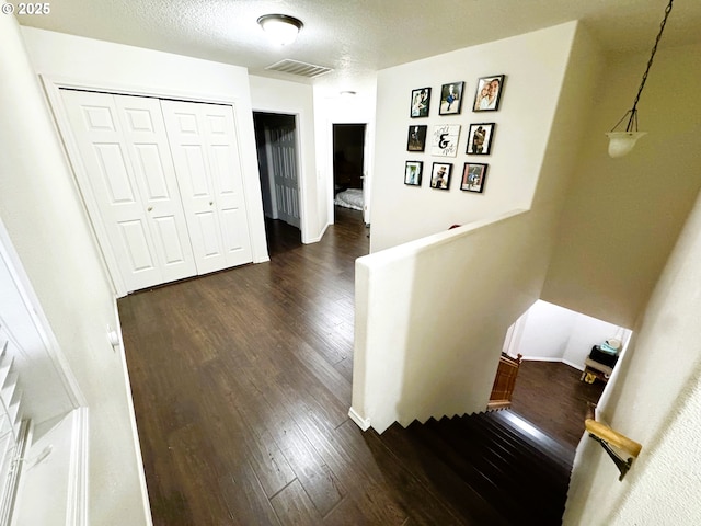 hallway with visible vents, a textured ceiling, dark wood finished floors, and an upstairs landing