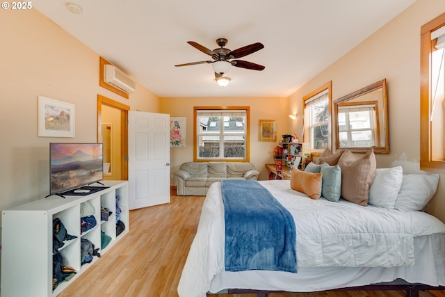 bedroom with ceiling fan, a wall unit AC, and light hardwood / wood-style floors