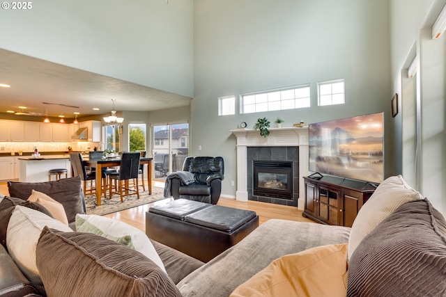 living room featuring an inviting chandelier, a towering ceiling, a fireplace, and light hardwood / wood-style floors