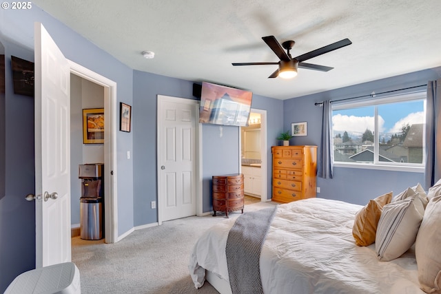 bedroom featuring ceiling fan, light colored carpet, ensuite bathroom, and a textured ceiling