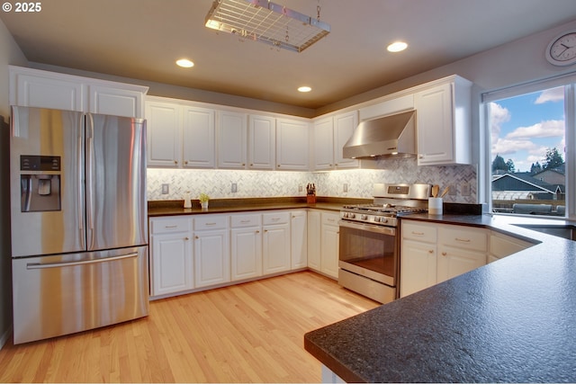 kitchen with appliances with stainless steel finishes, tasteful backsplash, white cabinets, light hardwood / wood-style floors, and wall chimney exhaust hood