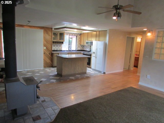 10285 S Rosewood Way, Molalla, OR 97038 - kitchen with appliances with stainless steel finishes, a wood stove, ceiling fan, light wood-style floors, and a center island