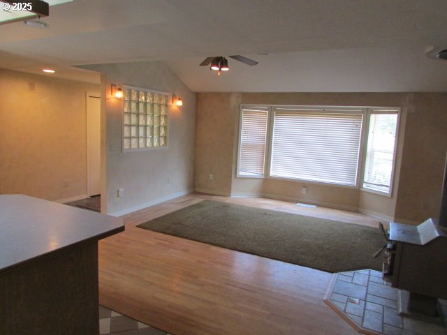 10285 S Rosewood Way, Molalla, OR 97038 - unfurnished living room with a ceiling fan, a wood stove, healthy amount of natural light, vaulted ceiling, and wood finished floors