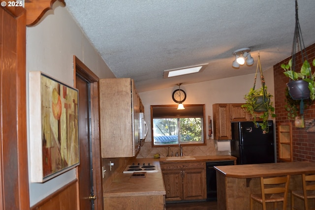 kitchen featuring vaulted ceiling with skylight, sink, a textured ceiling, and black appliances