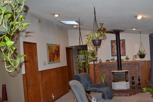 carpeted living room featuring vaulted ceiling with skylight, wood walls, a textured ceiling, and a wood stove