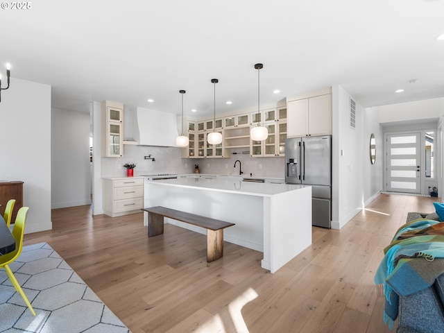 kitchen featuring wall chimney exhaust hood, tasteful backsplash, decorative light fixtures, high quality fridge, and a kitchen island