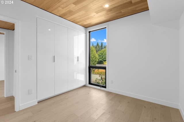 unfurnished bedroom featuring light wood-style flooring, wood ceiling, baseboards, and a closet