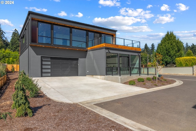 rear view of house featuring a garage, concrete driveway, a balcony, and fence