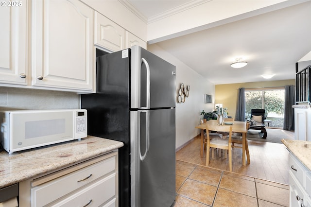 kitchen with light tile patterned floors, white microwave, freestanding refrigerator, ornamental molding, and white cabinetry