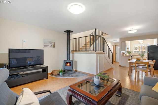 living room with stairs, a wood stove, and light wood-style floors