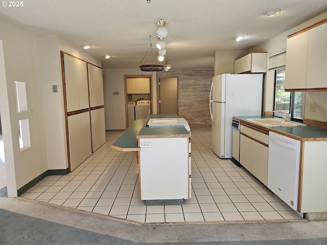 kitchen featuring white appliances, washer and dryer, a center island, a textured ceiling, and a sink