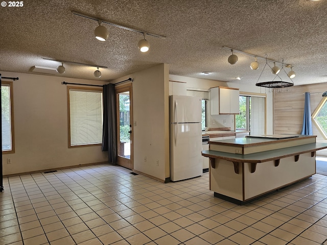 710 E Quince Ave, Hermiston, OR 97838 - kitchen featuring white appliances, white cabinetry, a textured ceiling, rail lighting, and a kitchen breakfast bar