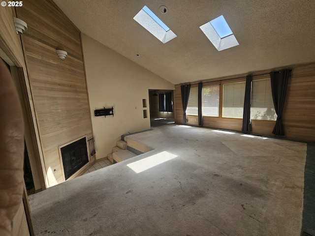 unfurnished living room with a skylight, a large fireplace, carpet floors, wood walls, and a textured ceiling