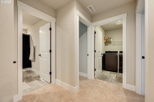 corridor featuring washer and clothes dryer, visible vents, baseboards, and carpet