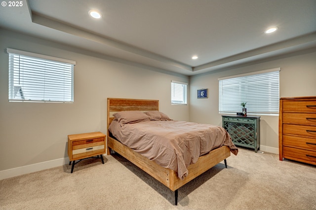 bedroom featuring a tray ceiling, light carpet, and baseboards