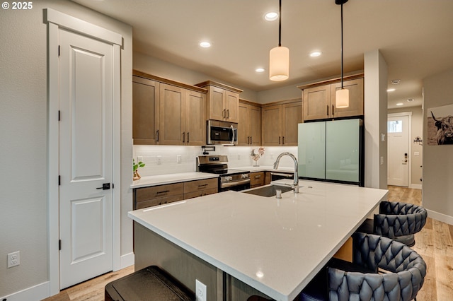 kitchen with light wood-type flooring, a sink, a kitchen breakfast bar, appliances with stainless steel finishes, and decorative backsplash