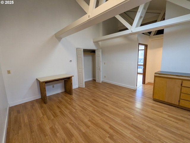 unfurnished living room featuring baseboards, light wood-style floors, and high vaulted ceiling