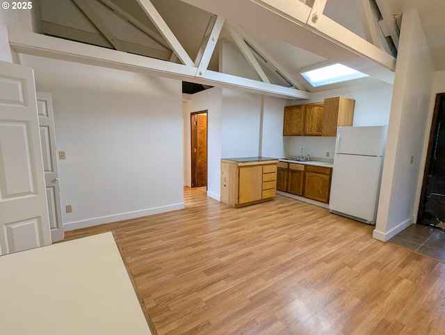 kitchen featuring a sink, freestanding refrigerator, light wood-style floors, brown cabinetry, and light countertops