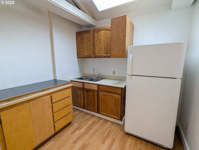 kitchen featuring brown cabinetry, lofted ceiling, freestanding refrigerator, a sink, and light wood-type flooring