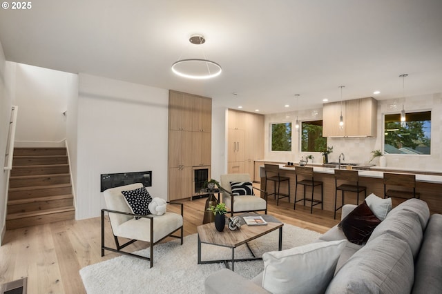 living room featuring a glass covered fireplace, stairway, visible vents, and light wood finished floors