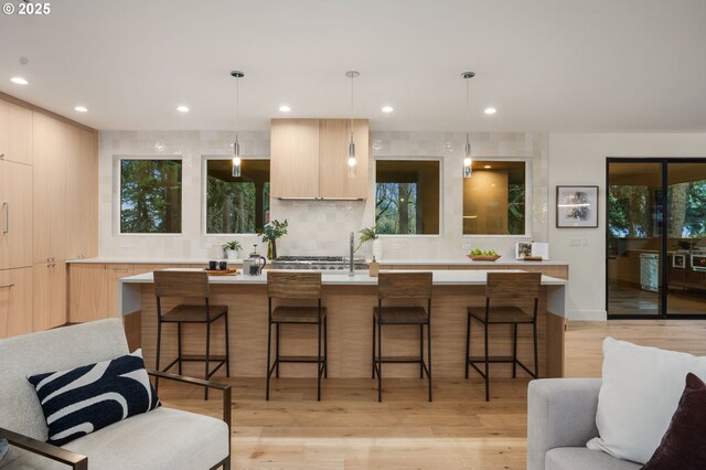 kitchen with light brown cabinetry, a center island with sink, a kitchen breakfast bar, modern cabinets, and a sink