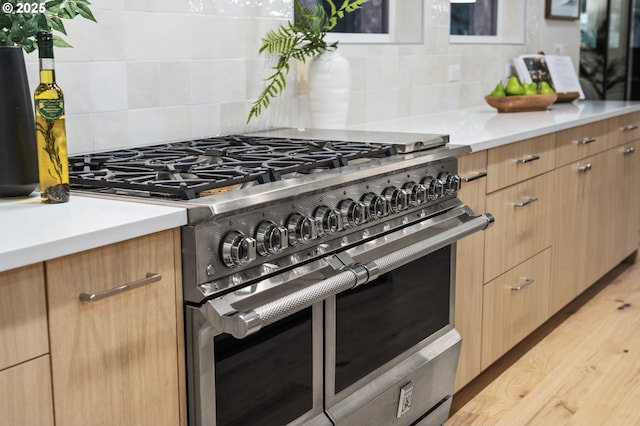 kitchen with backsplash, double oven range, light wood-type flooring, light countertops, and modern cabinets