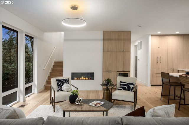 living area featuring a glass covered fireplace, stairway, recessed lighting, and light wood finished floors