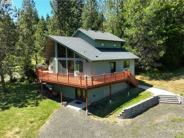 rear view of property featuring gravel driveway, a deck, a yard, and a shingled roof