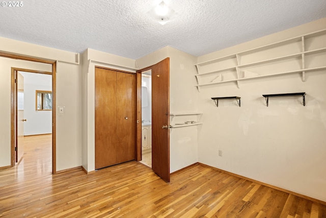 unfurnished bedroom with a textured ceiling, light wood finished floors, and a closet