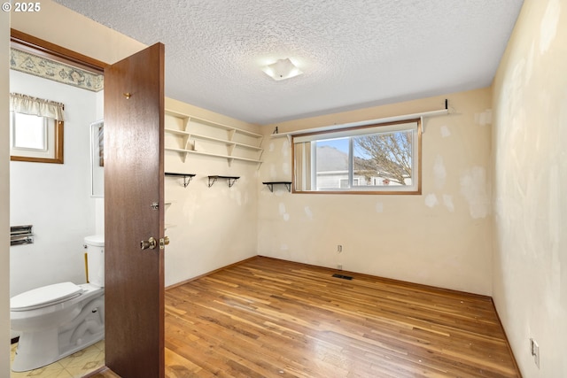 bathroom with a textured ceiling, visible vents, wood finished floors, and toilet