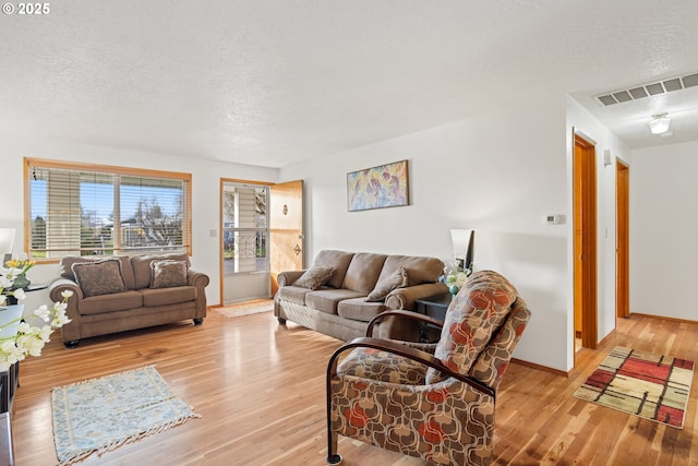 living room featuring baseboards, visible vents, light wood-style flooring, and a textured ceiling