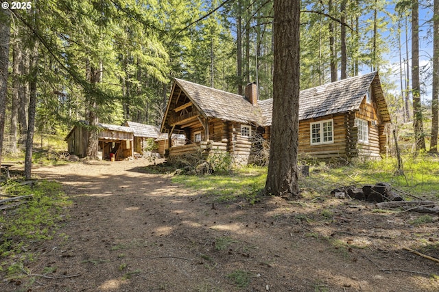view of property exterior with log siding, a chimney, a storage unit, and an outdoor structure