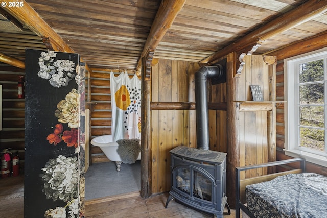 bedroom with multiple windows, wood ceiling, a wood stove, log walls, and hardwood / wood-style flooring