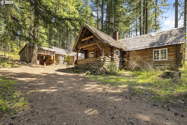 back of house with a chimney, log exterior, and an outbuilding