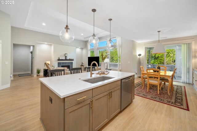 kitchen with a tiled fireplace, stainless steel dishwasher, a sink, and light wood-style floors