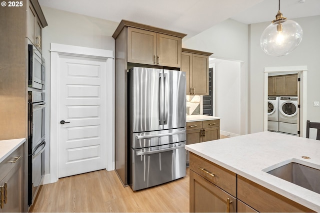 kitchen with light wood finished floors, stainless steel appliances, a sink, washing machine and dryer, and pendant lighting