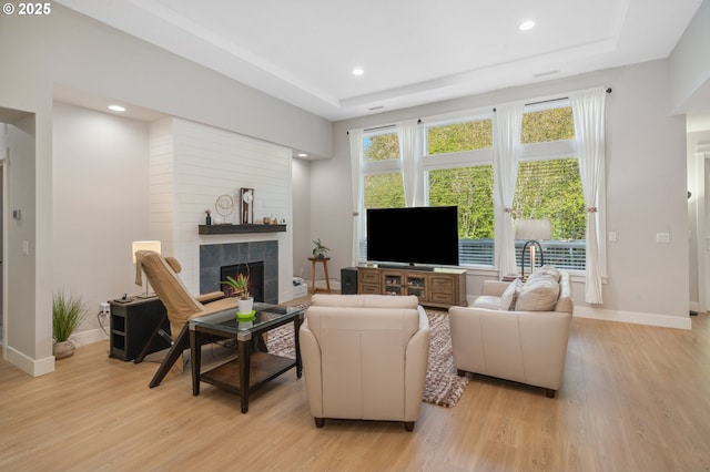 living area featuring recessed lighting, light wood finished floors, a raised ceiling, baseboards, and a tiled fireplace