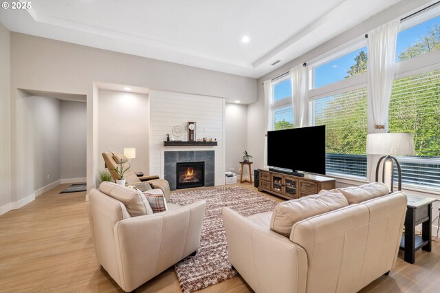 living area with light wood-style floors, a fireplace, a raised ceiling, baseboards, and recessed lighting