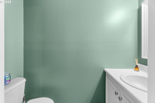half bath featuring toilet, vanity, and a textured wall