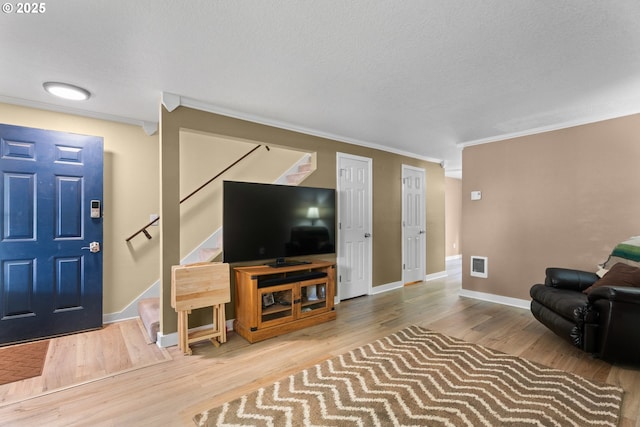 living area with stairs, ornamental molding, wood finished floors, baseboards, and a textured ceiling