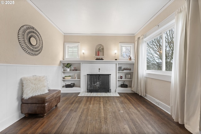 living area with wainscoting, dark wood-style flooring, a fireplace, and crown molding