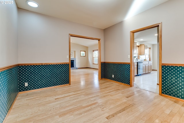 spare room with light wood-style flooring, a fireplace with raised hearth, and wainscoting