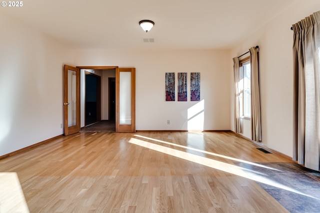 spare room featuring light wood-type flooring, visible vents, and baseboards