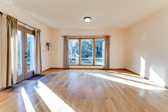 empty room with french doors, light wood-style flooring, and baseboards