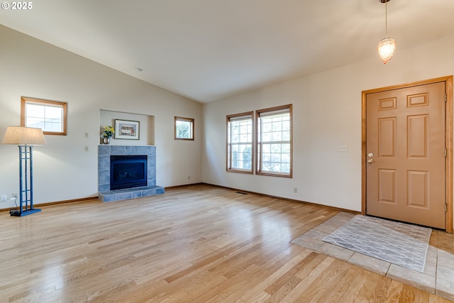 foyer with lofted ceiling, light wood-style flooring, baseboards, and a tiled fireplace