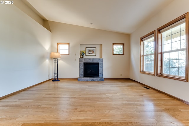 unfurnished living room with light wood finished floors, lofted ceiling, visible vents, a tiled fireplace, and baseboards