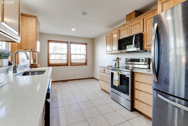 kitchen with appliances with stainless steel finishes, light tile patterned flooring, a sink, light stone countertops, and baseboards