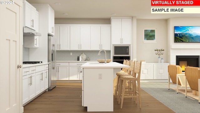 kitchen with a center island with sink, a sink, a tile fireplace, under cabinet range hood, and black appliances