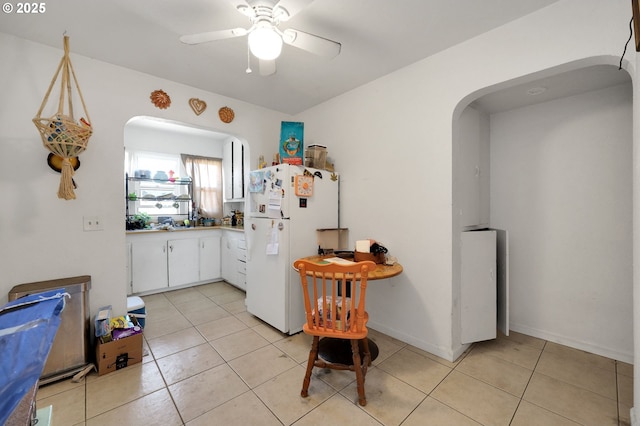 kitchen with a ceiling fan, freestanding refrigerator, light tile patterned flooring, white cabinets, and arched walkways