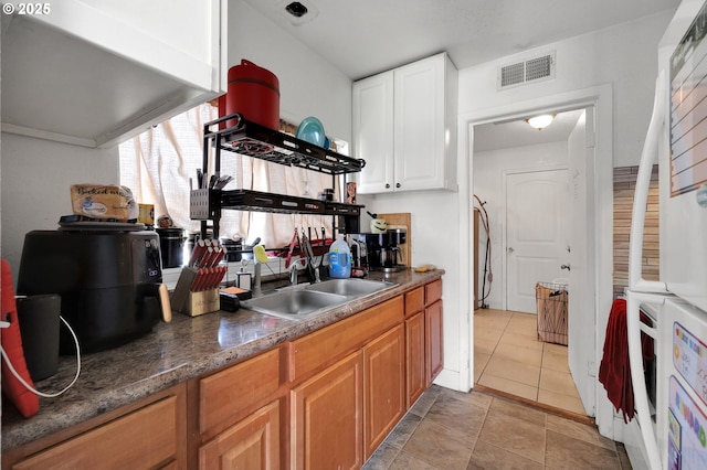 kitchen featuring visible vents, freestanding refrigerator, light tile patterned flooring, white cabinets, and a sink